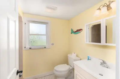 A small bathroom with a toilet, sink, and decorative mermaid tail on the wall.