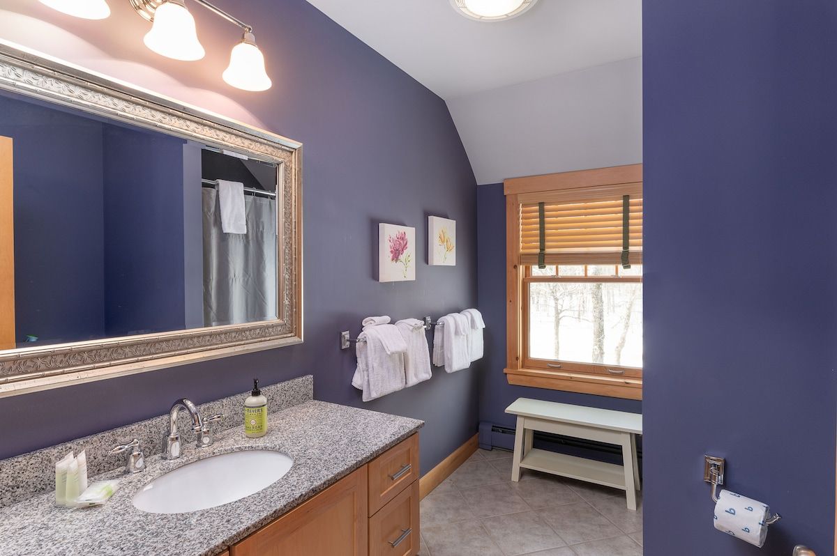 A clean and well-lit bathroom with a large mirror, granite countertop, and a window overlooking the outdoors.