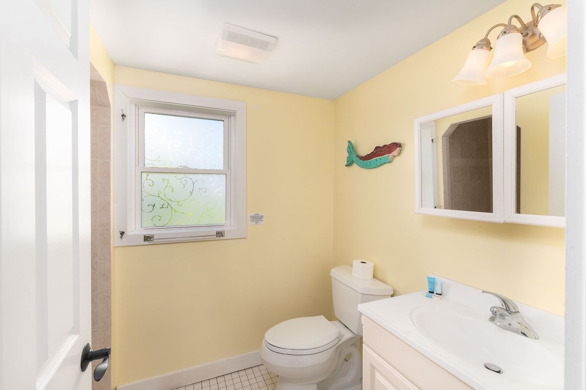 A small bathroom with a toilet, sink, and decorative mermaid tail on the wall.