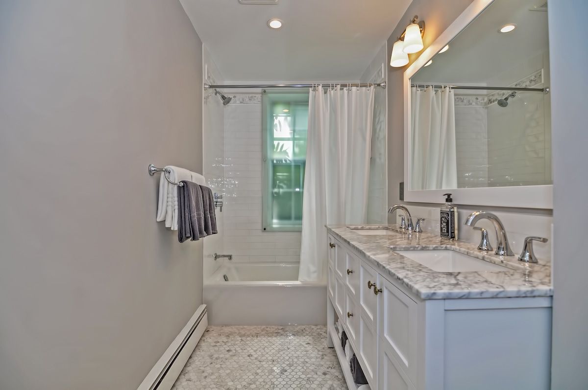 A clean and modern bathroom with a white bathtub, marble countertops, and a large mirror.
