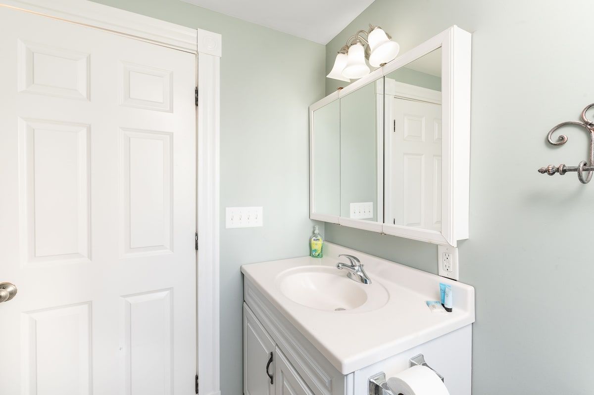 A clean and well-lit bathroom with a white vanity, mirror, and light fixture.
