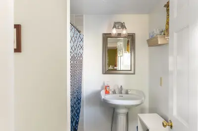 A small bathroom with a pedestal sink and mirror, featuring a soap dispenser on the counter.