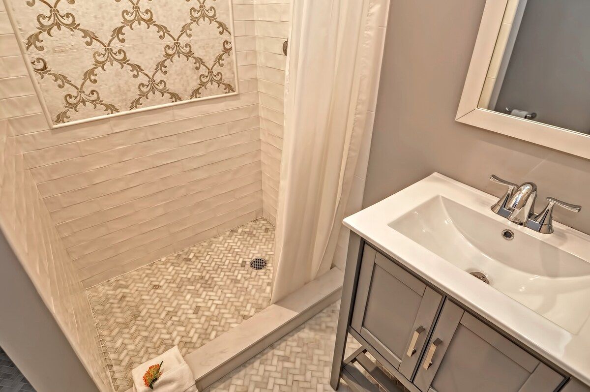 A modern bathroom with a white sink and shower, featuring decorative tile work on the walls.