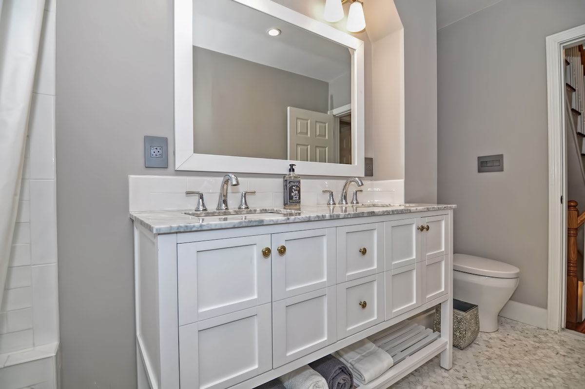 A modern bathroom with a white vanity, marble countertop, and a large mirror.