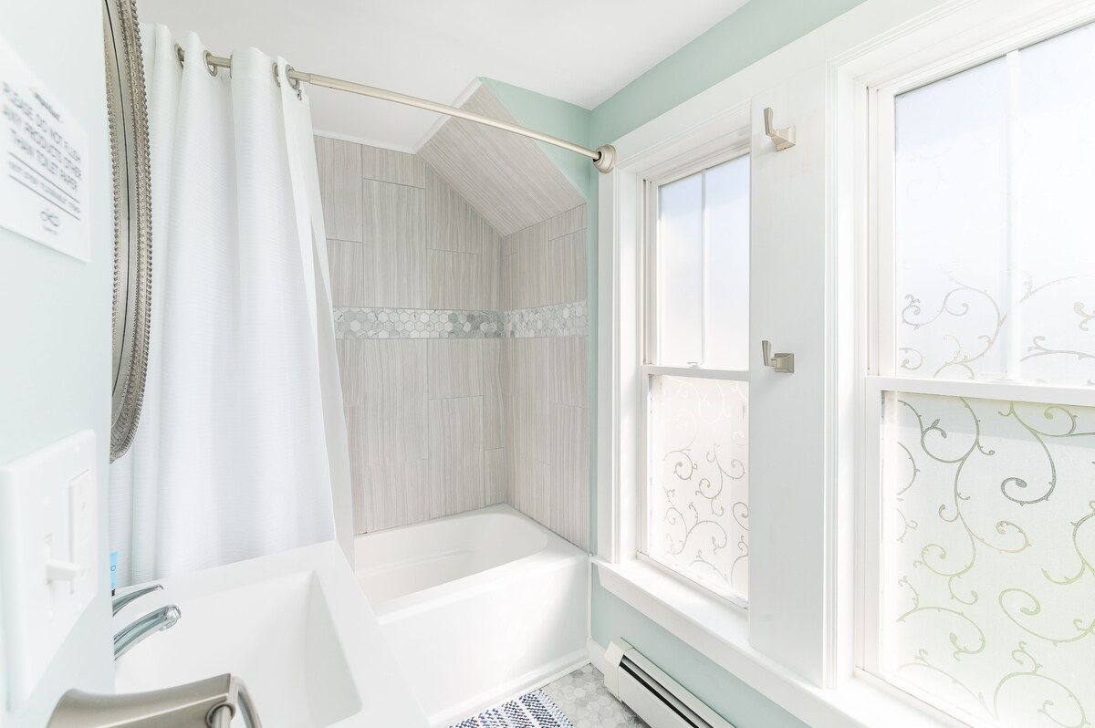 A clean and modern bathroom with a bathtub, shower curtain, and natural light from the window.