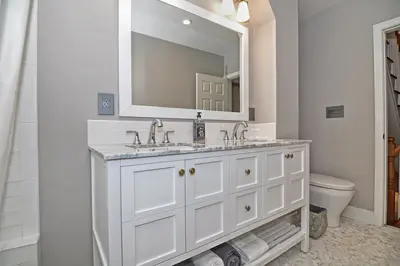 A modern bathroom with a white vanity, marble countertop, and a large mirror.