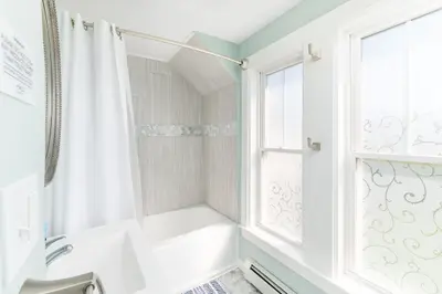 A clean and modern bathroom with a bathtub, shower curtain, and natural light from the window.