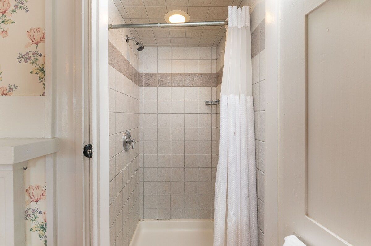 A clean and well-lit bathroom with a shower, bathtub, and white curtain.