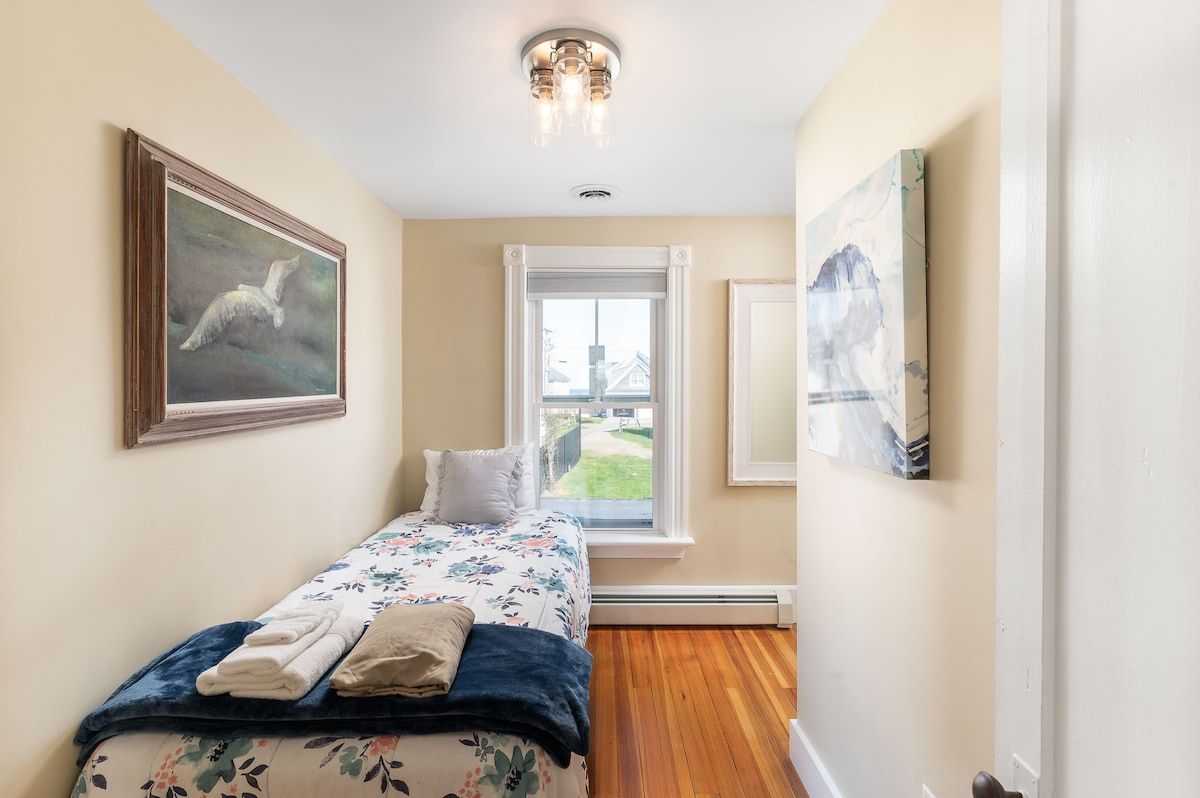 Cozy single bed with floral bedding and a window overlooking the neighborhood