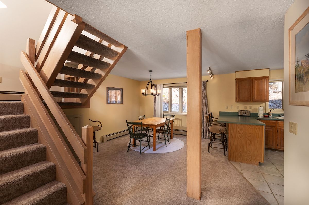 A cozy dining area with a wooden table and chairs, surrounded by warm lighting and natural light from the windows.