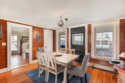 A cozy dining area with a wooden table and chairs, surrounded by windows offering a view of the outside.