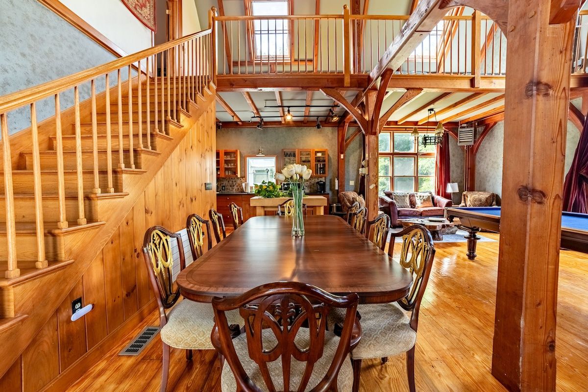 A spacious dining area with a large wooden table and chairs, surrounded by windows offering a view of the outdoors.
