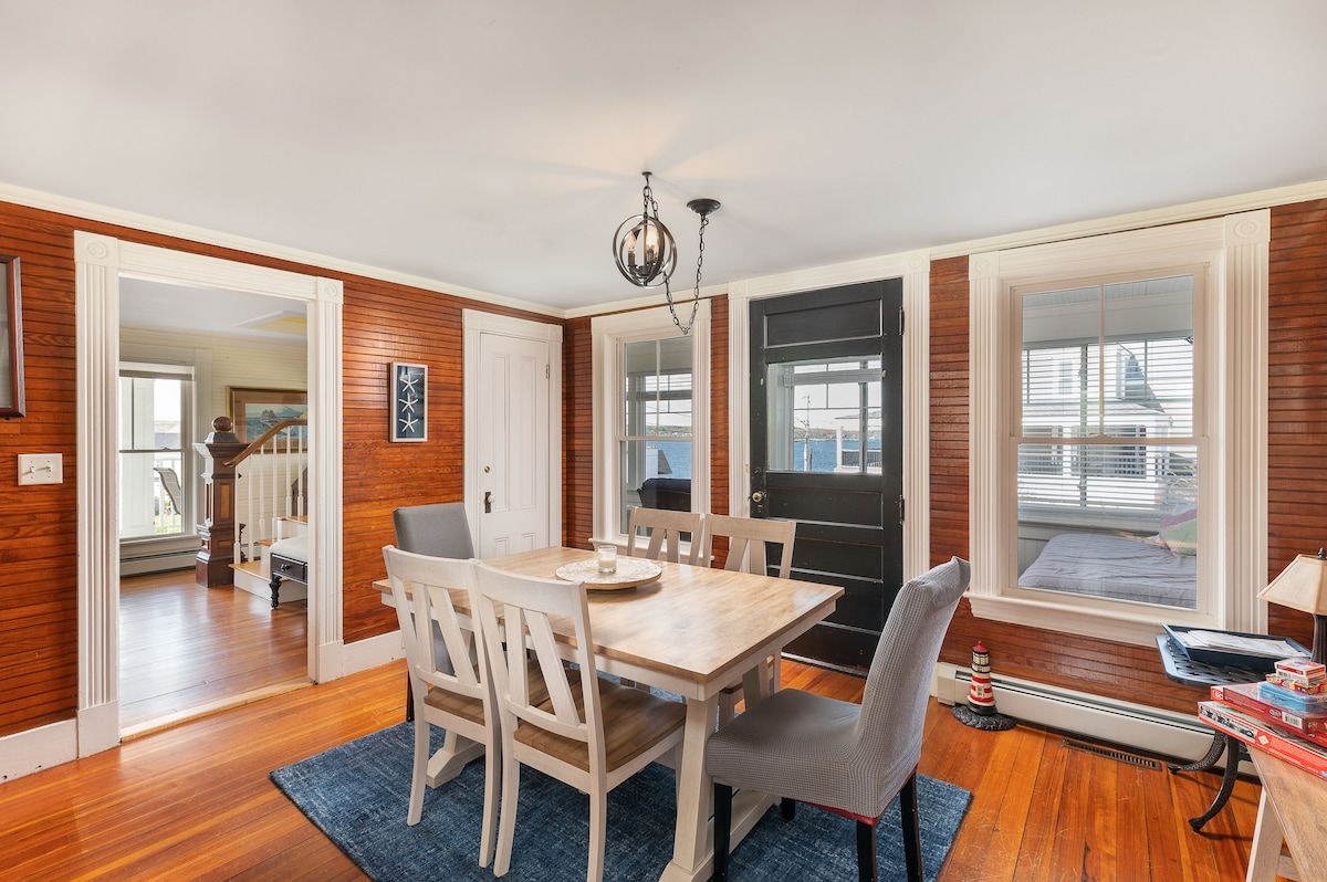 A cozy dining area with a wooden table and chairs, surrounded by windows offering a view of the outside.