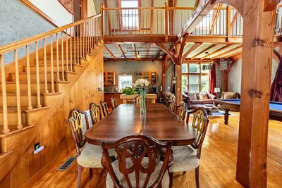 A spacious dining area with a large wooden table and chairs, surrounded by windows offering a view of the outdoors.