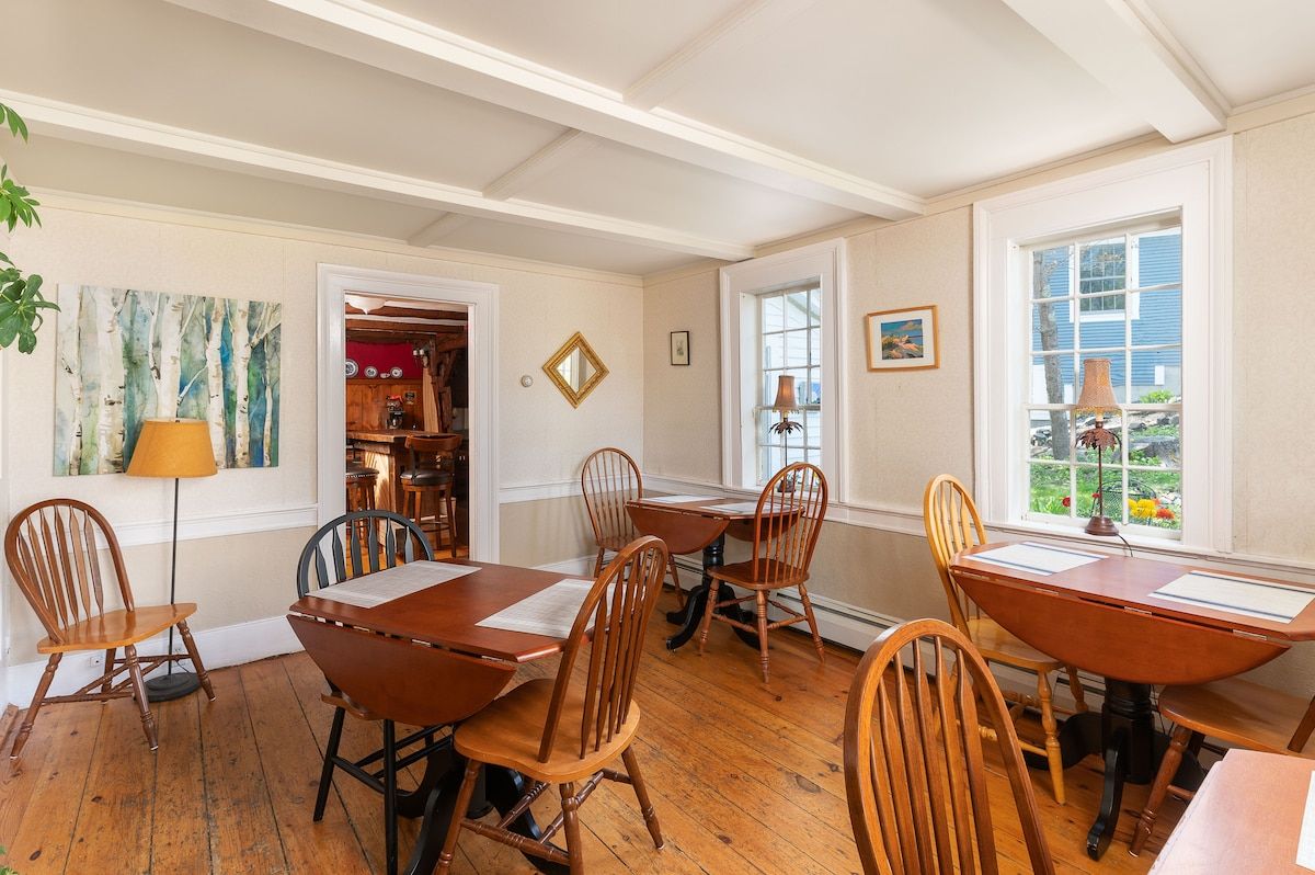 A spacious dining room with a large wooden table and chairs, surrounded by windows and a beautiful view.