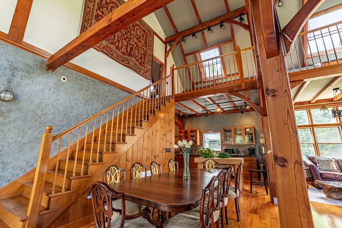 A spacious dining area with a large wooden table and chairs, surrounded by windows offering a view of the outdoors.