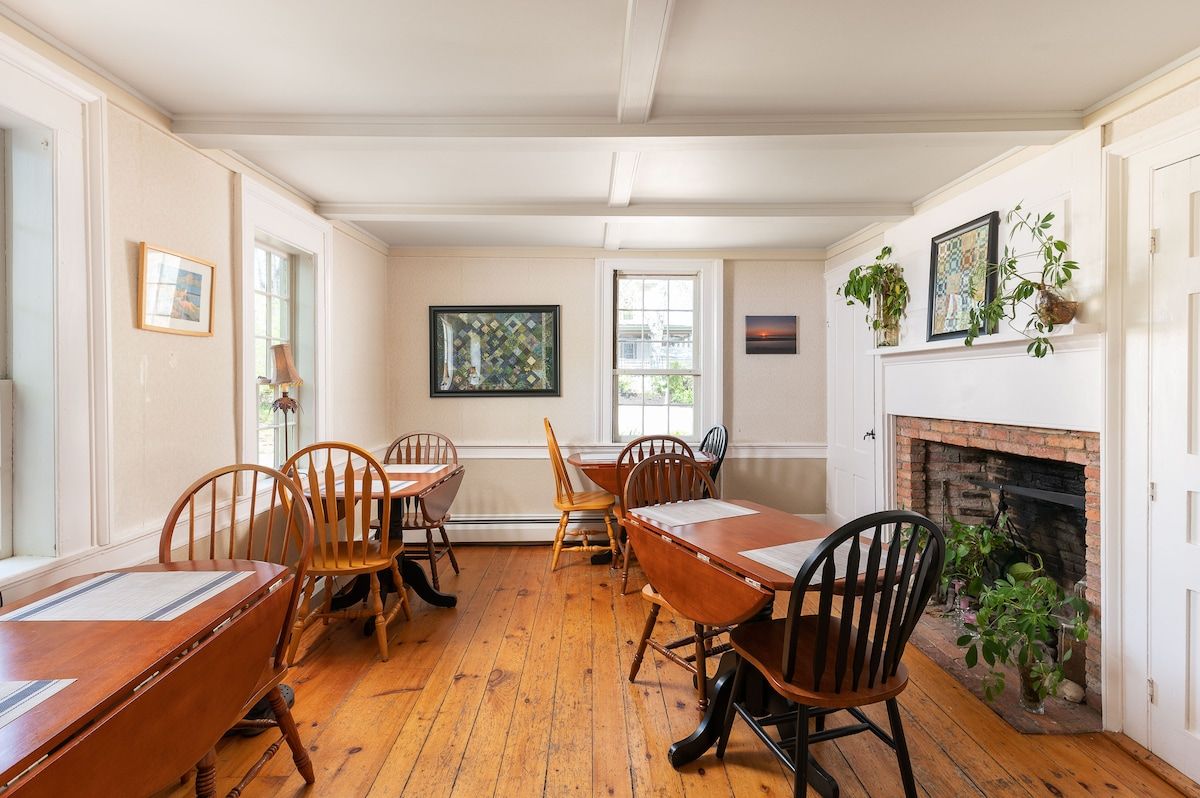A spacious dining room with a large wooden table and chairs, surrounded by windows and a fireplace.