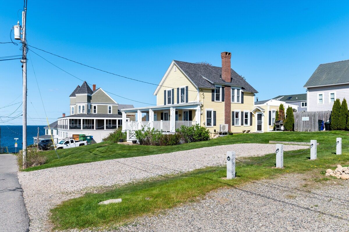 A large house with a porch and chimney, overlooking the ocean.
