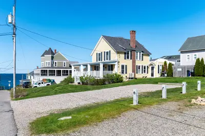 A large house with a porch and chimney, overlooking the ocean.