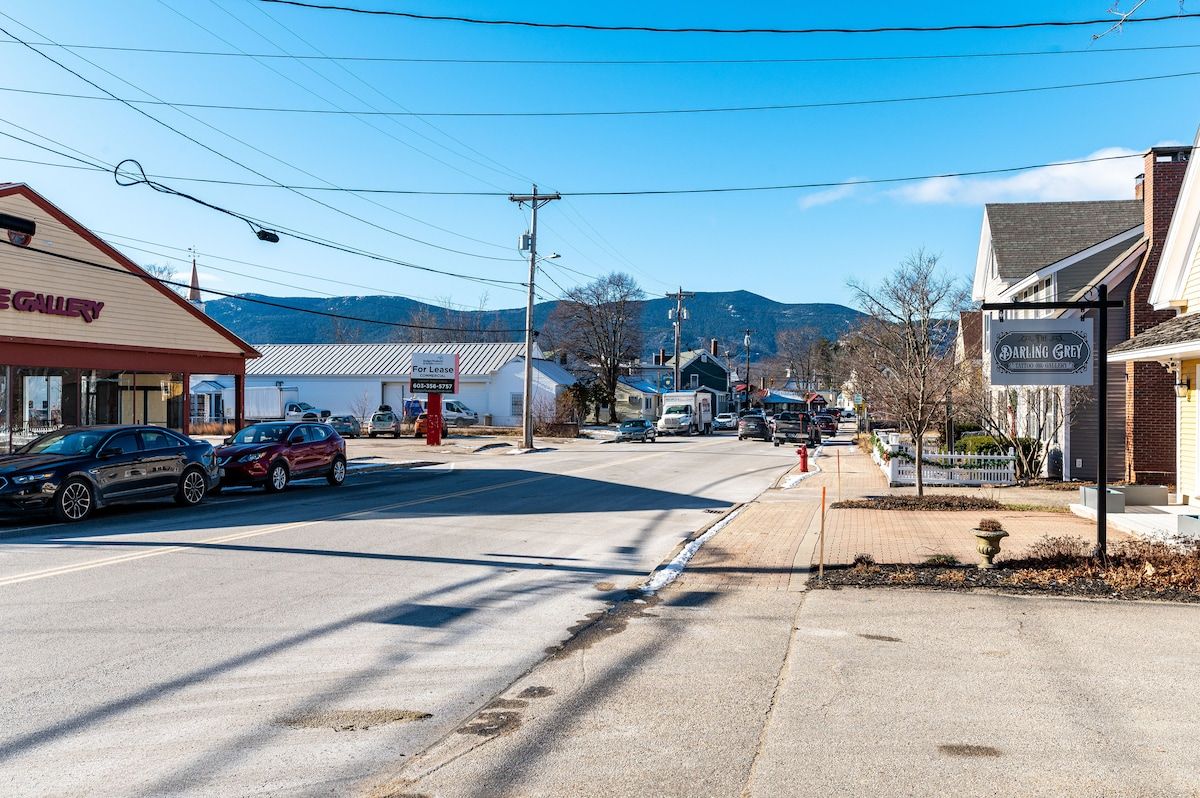 A small town street with a few shops and cars parked along the side of the road.