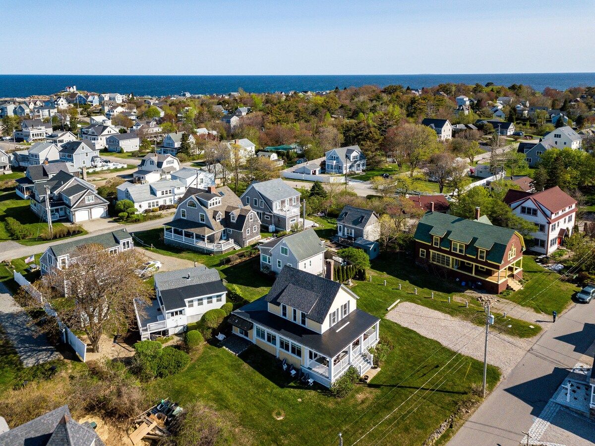 Aerial view of a coastal neighborhood with houses and trees, featuring a large body of water in the background.