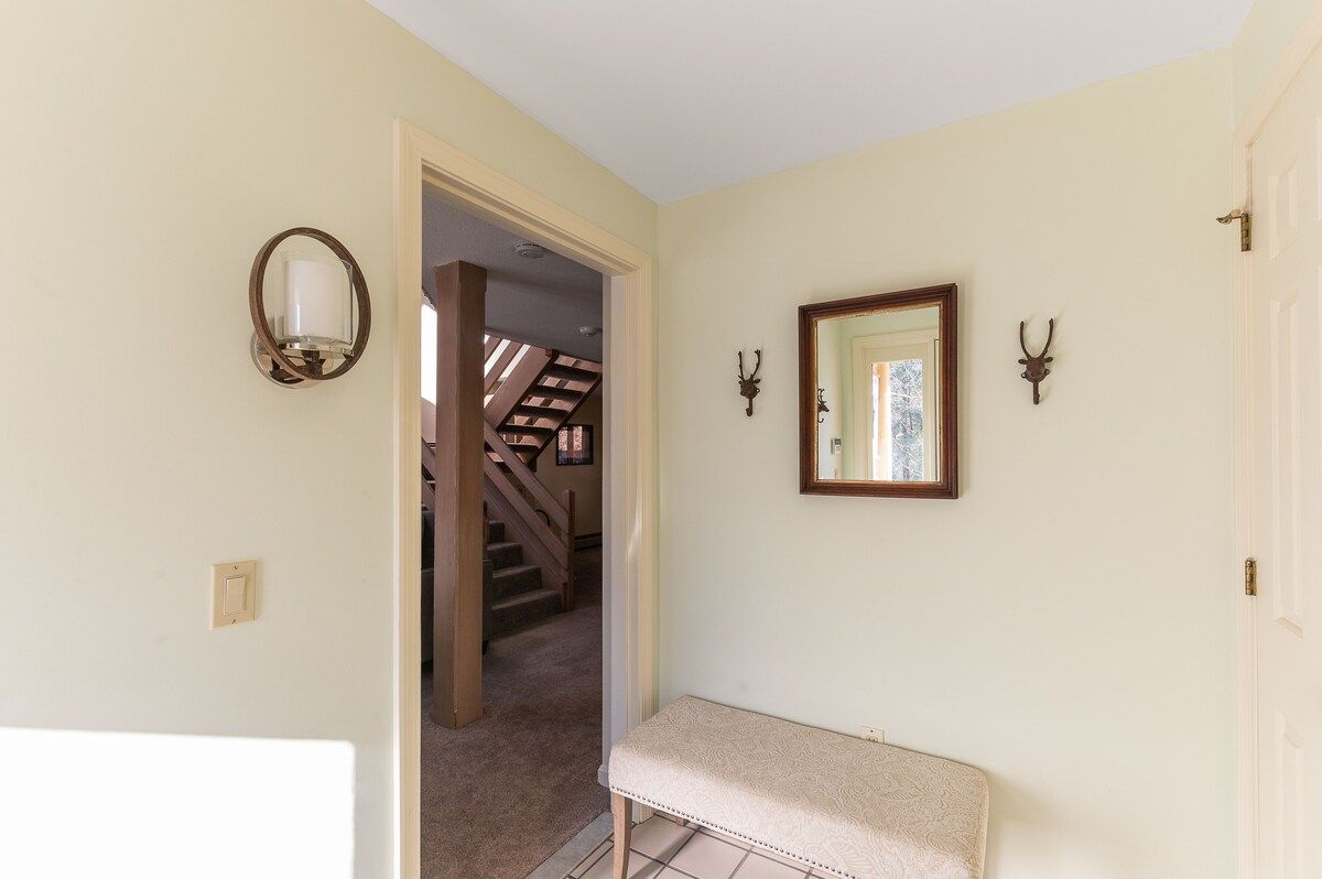 A bench and mirror in a hallway with stairs leading to the second floor.