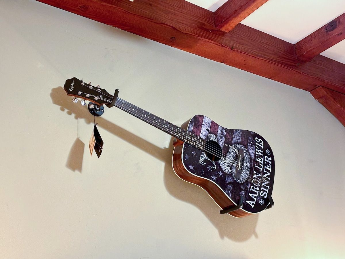 A guitar hangs on a wall in a cozy room with exposed wooden beams.