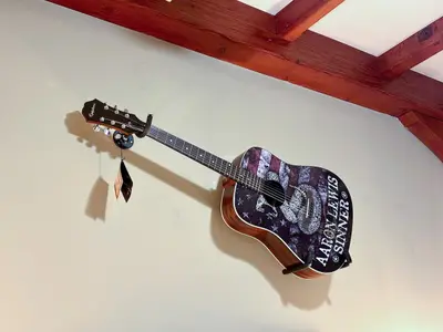 A guitar hangs on a wall in a cozy room with exposed wooden beams.