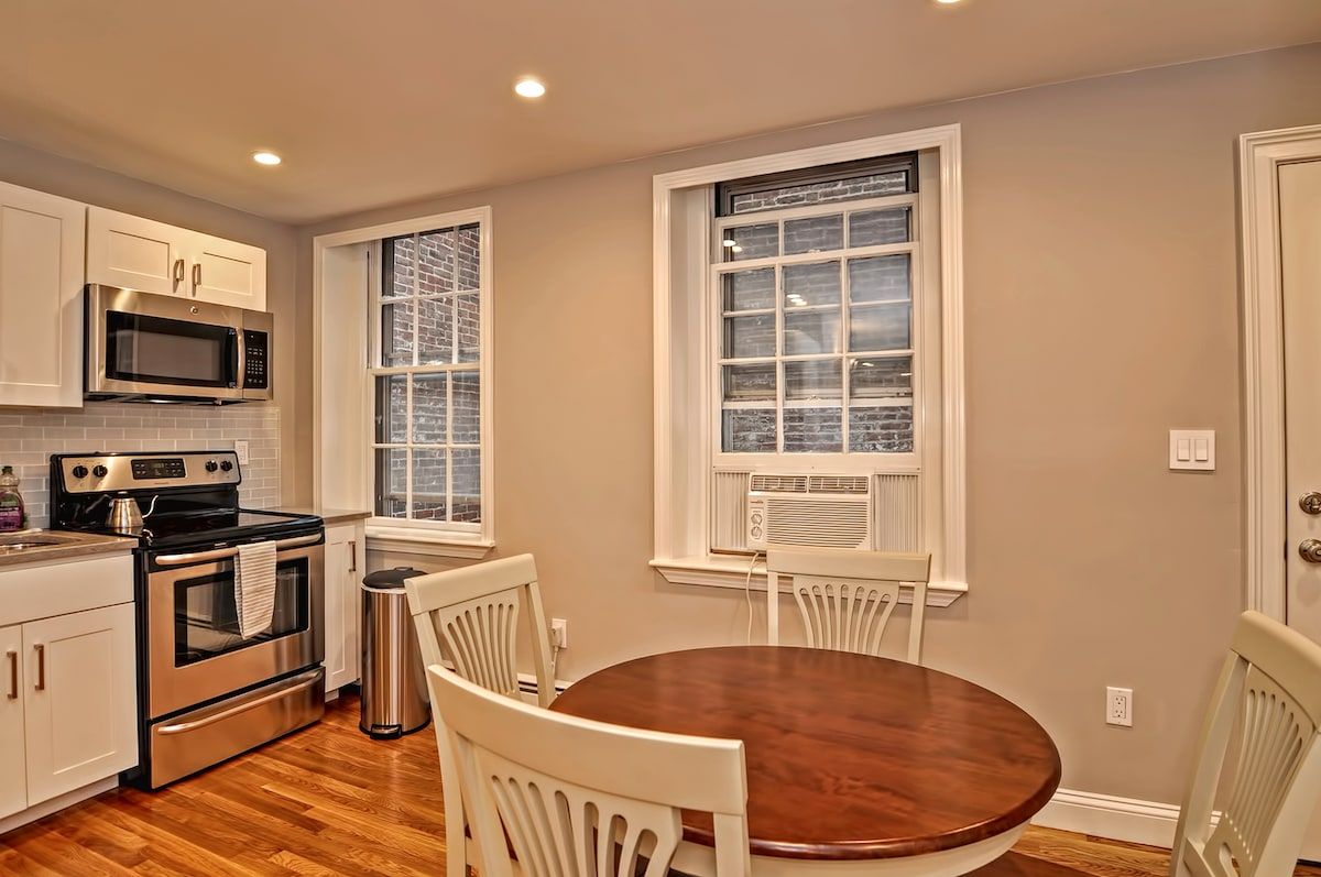 A small kitchen with a stainless steel stove and microwave, white cabinets, and a wooden table in the dining area.