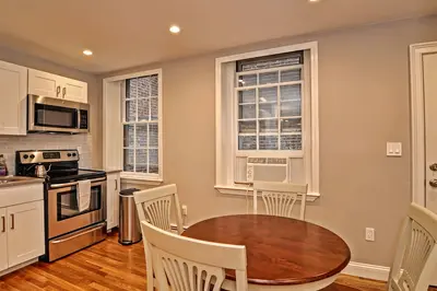 A small kitchen with a stainless steel stove and microwave, white cabinets, and a wooden table in the dining area.