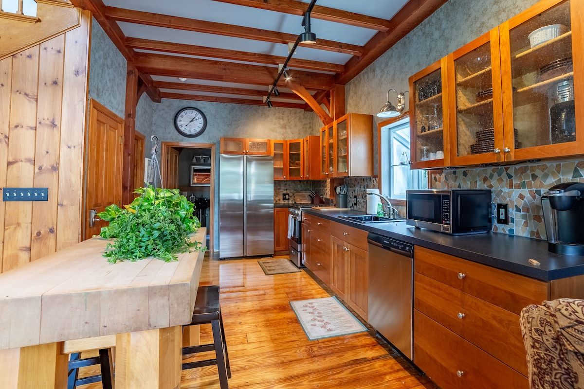 A well-equipped kitchen with stainless steel appliances and wooden cabinets, featuring a large island with a plant on top.