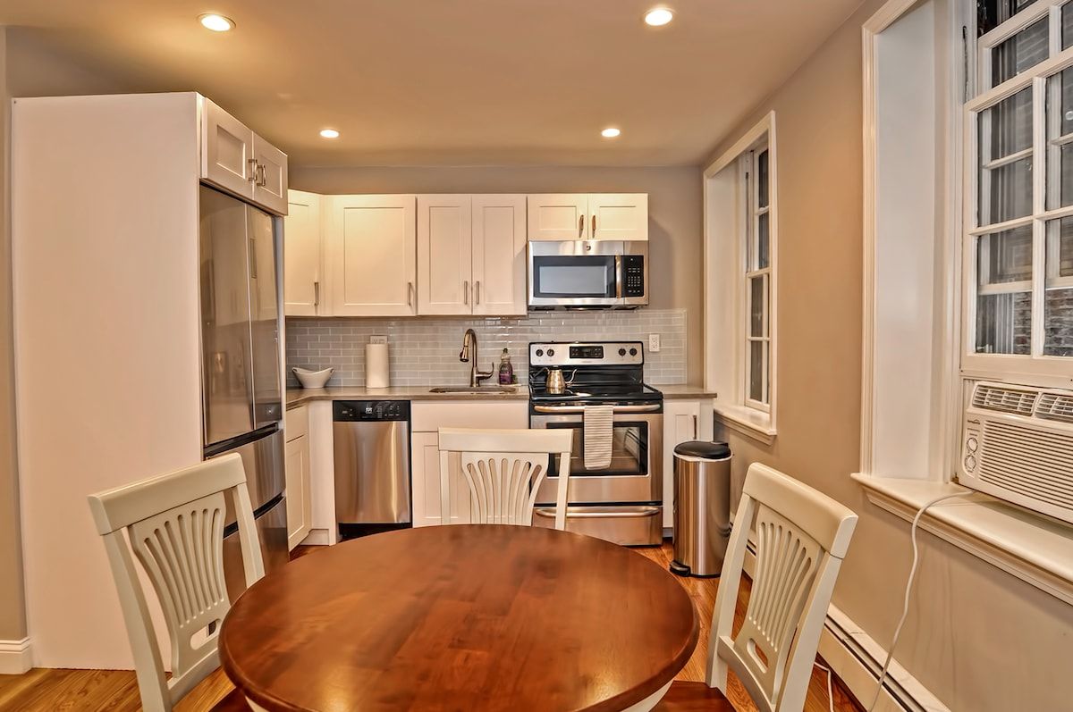 A compact kitchen with stainless steel appliances and white cabinets, featuring a microwave, stove, sink, and refrigerator.