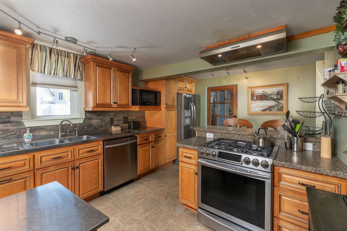 A well-equipped kitchen with stainless steel appliances and granite countertops, featuring a range, refrigerator, sink, and microwave.
