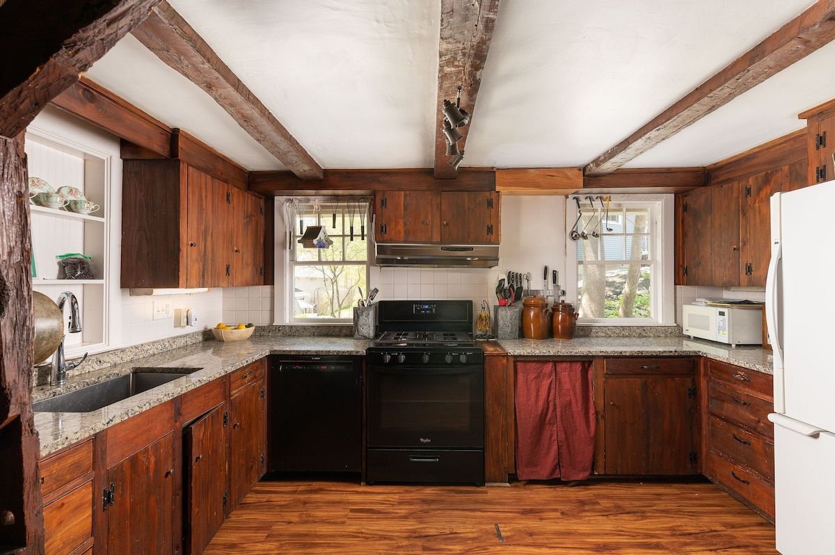 A rustic kitchen with dark wood cabinets and granite countertops, featuring a black stove and white refrigerator.