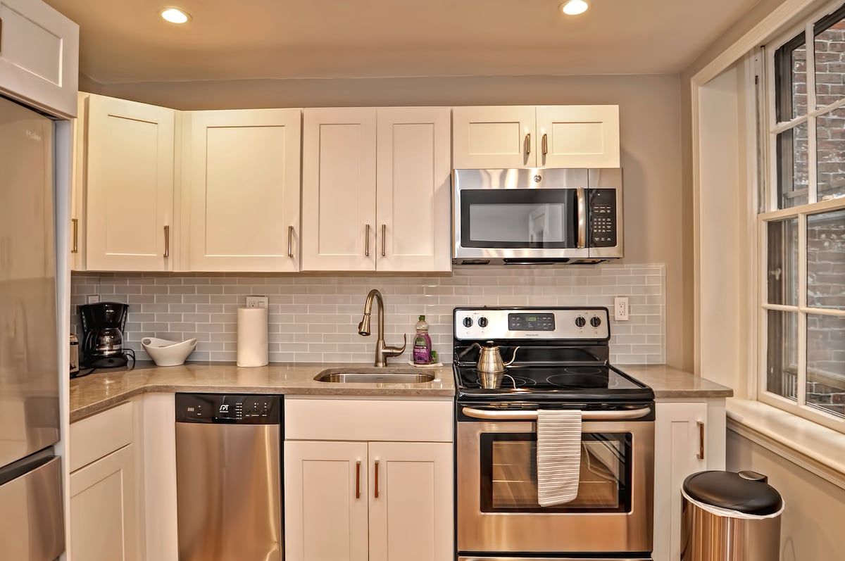 A modern kitchen with stainless steel appliances and white cabinets, featuring a window on the right side.