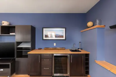 A compact kitchenette with a sink, wine fridge, and countertop in a cozy room.