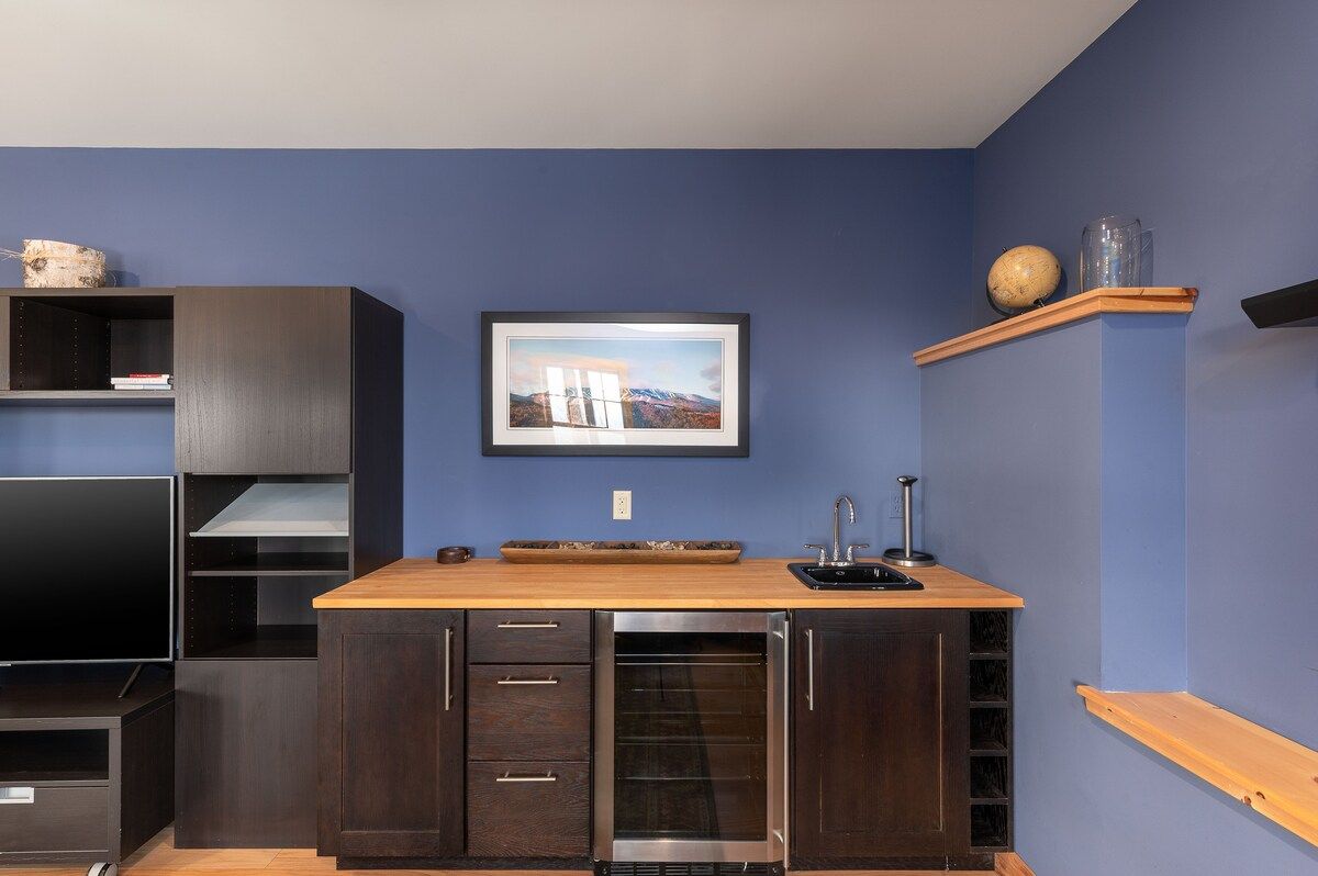 A compact kitchenette with a sink, wine fridge, and countertop in a cozy room.
