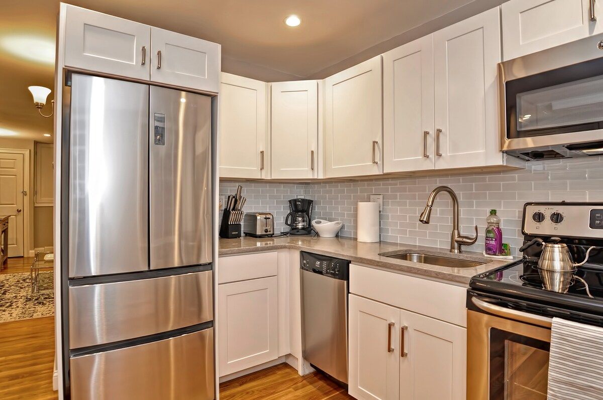 A modern kitchen with stainless steel appliances and white cabinets, featuring a refrigerator, stove, sink, and countertops.