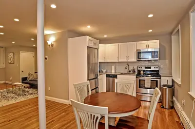 A modern kitchen with stainless steel appliances and white cabinets, featuring a round dining table in the foreground.