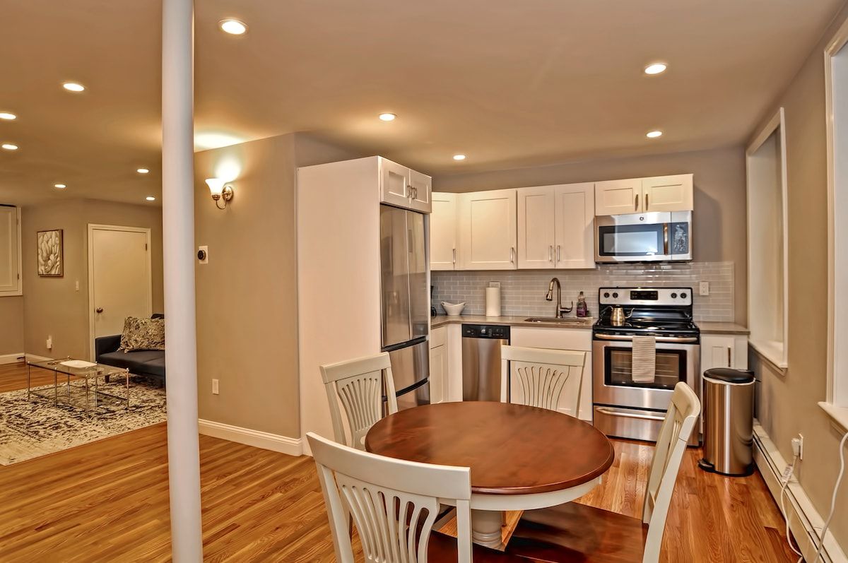 A modern kitchen with stainless steel appliances and white cabinets, featuring a round dining table in the foreground.