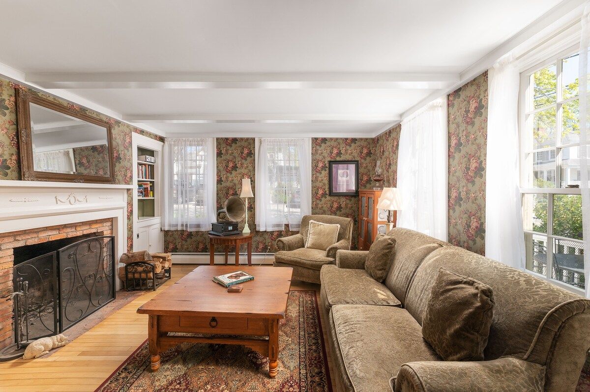 Cozy living room with a fireplace, comfortable sofa and armchair, and large windows.