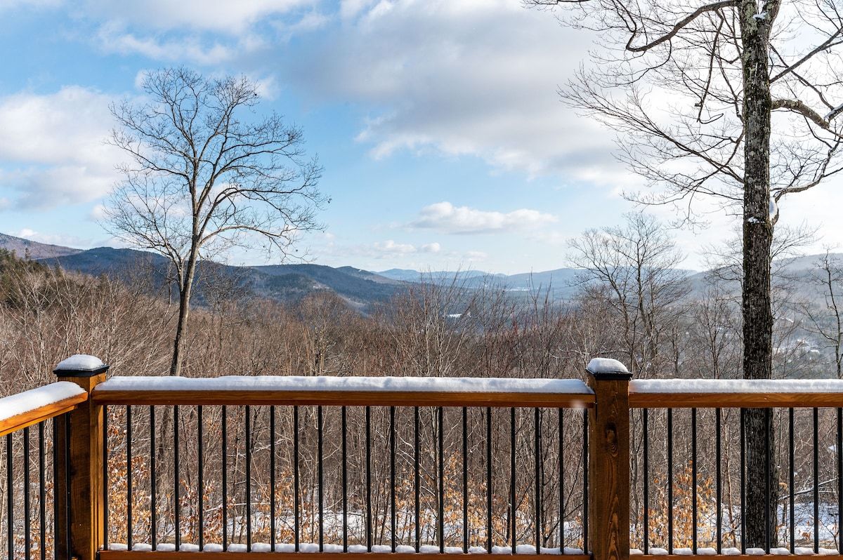 A snow-covered deck with a view of the mountains and trees in the background.