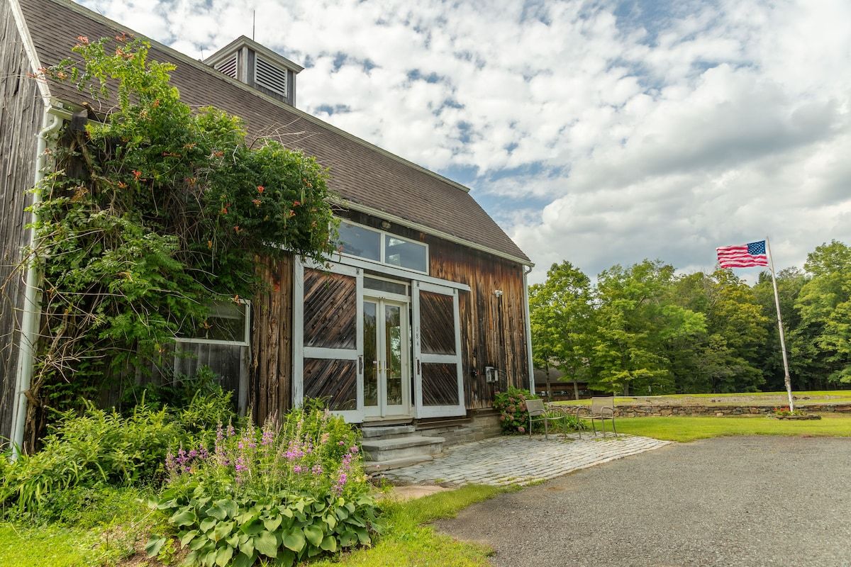 A large wooden barn with a flagpole and American flag in the yard.