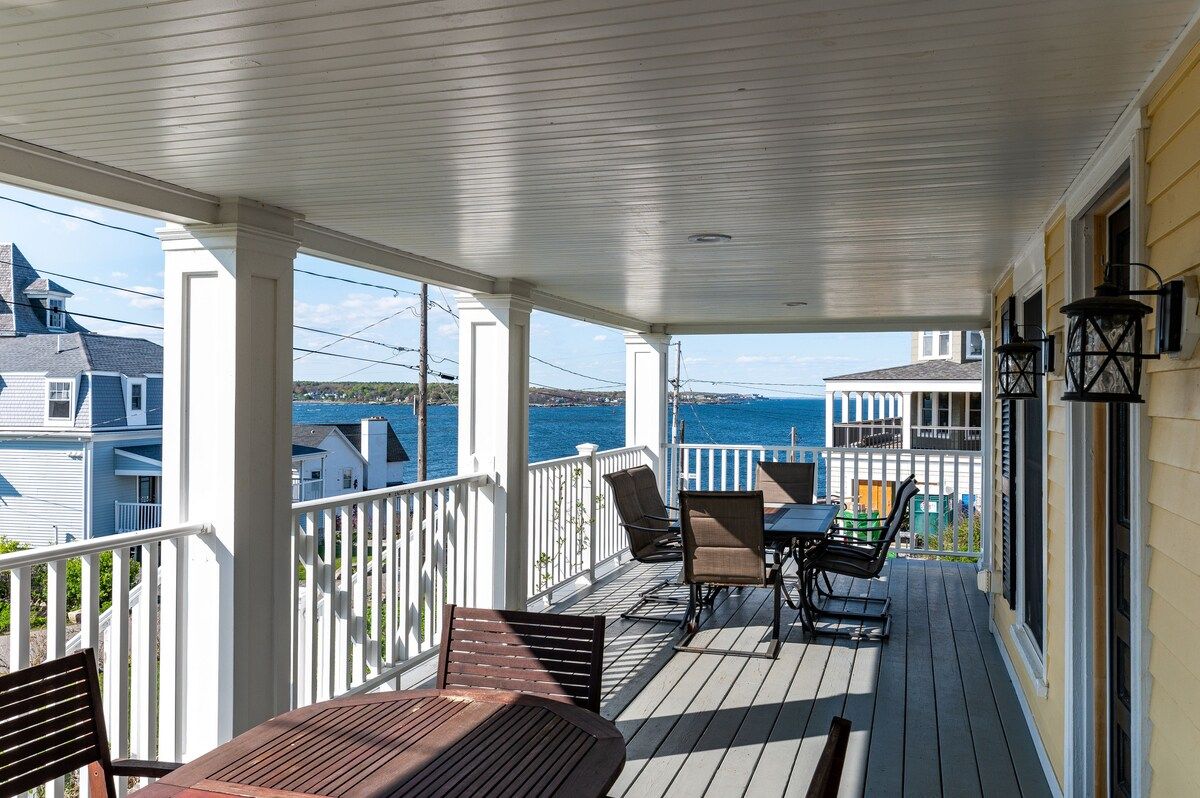 A spacious covered porch with a table and chairs overlooking the ocean.