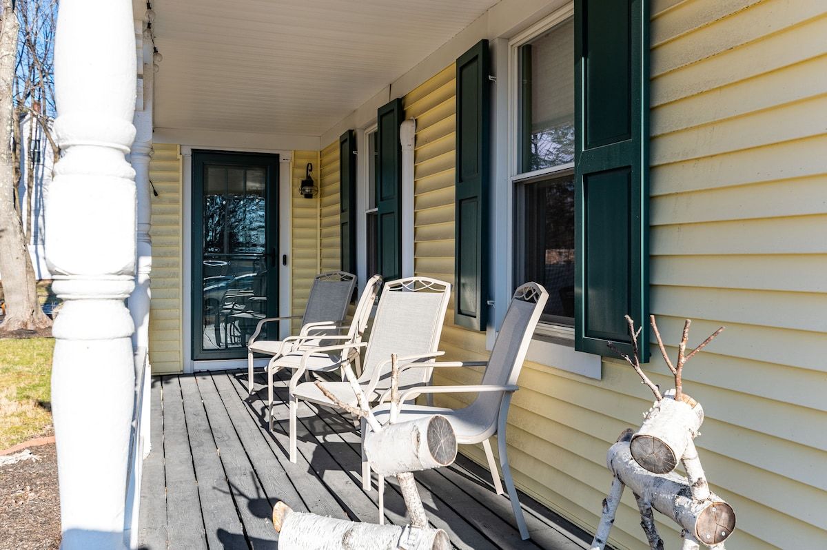 A cozy porch with white chairs and a reindeer decoration on the front of a house.