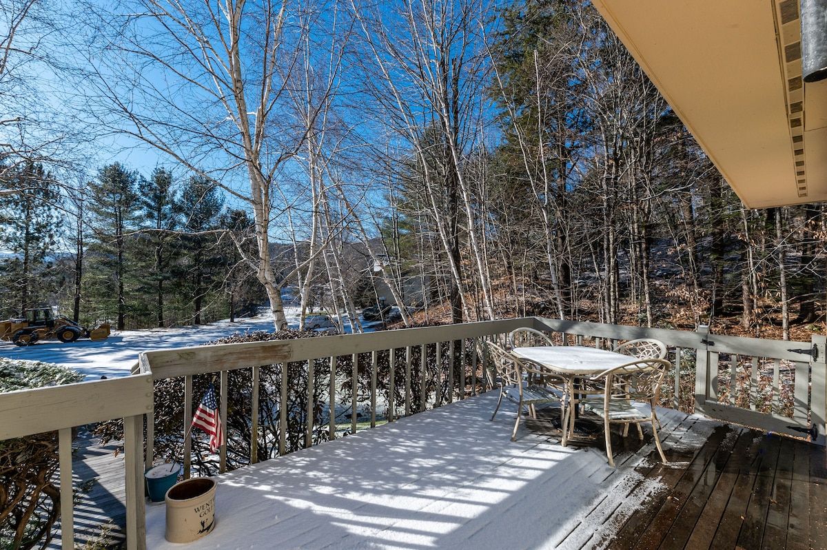 A snowy deck with a table and chairs overlooking the woods.