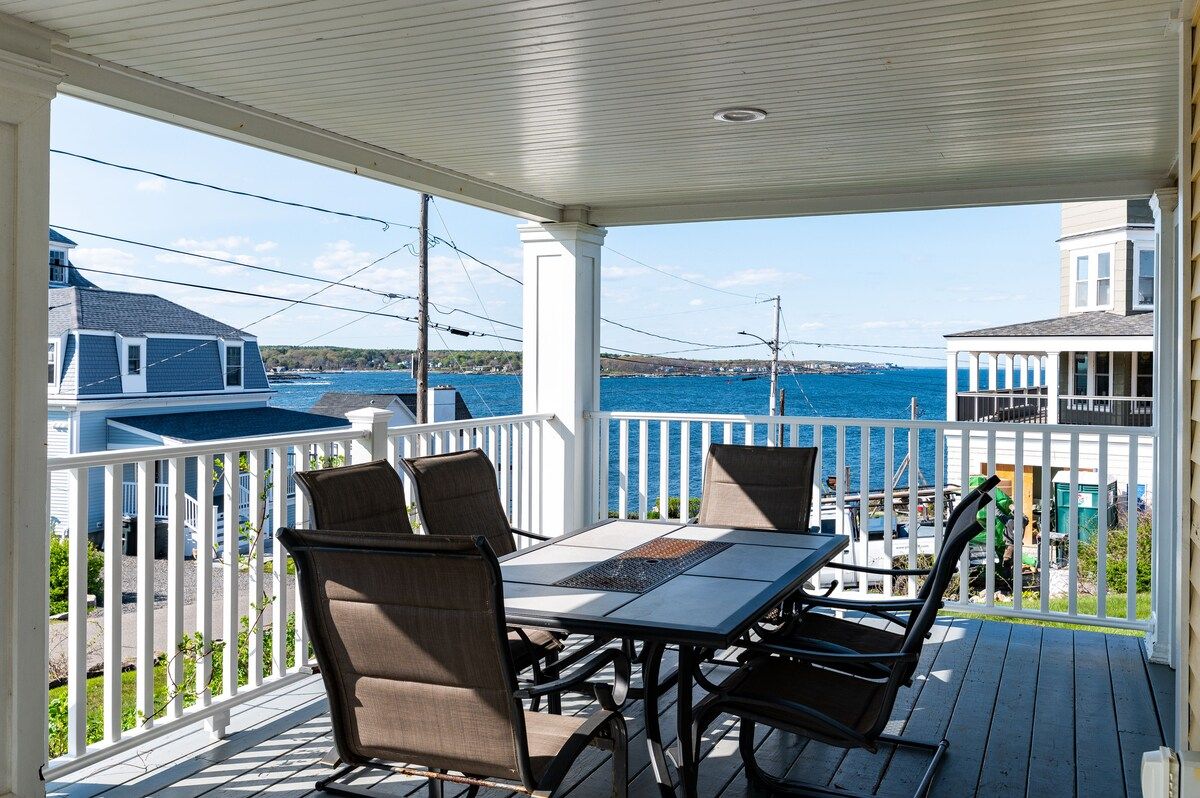 A covered porch with a table and chairs overlooking the ocean.