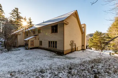 Snowy backyard with a large house and trees in the background