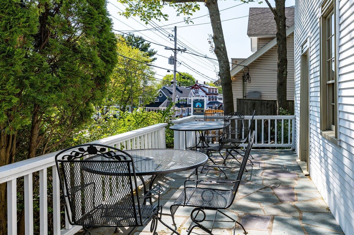 A cozy patio area with a table and chairs, surrounded by trees and houses in the background.