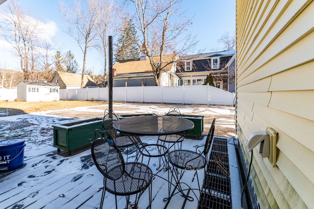 A snowy deck with a table and chairs, surrounded by houses in the background.